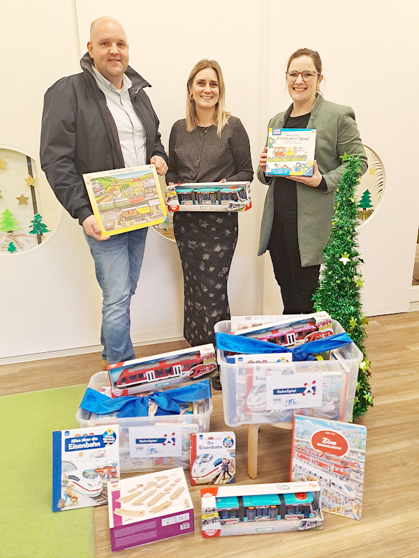 Drei Personen stehen hinter einen BahnSpielBox, jede hält ein Teil aus dem Inhalt der Box in der Hand