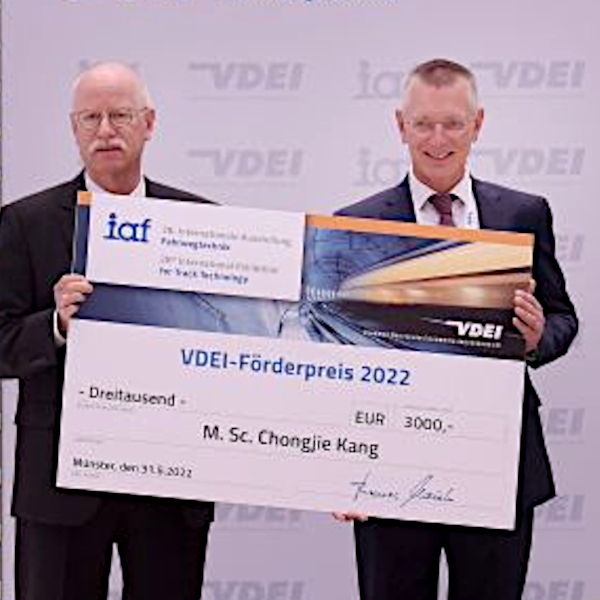 Zwei Personen auf einer halten einen vergrößerten symbolischen Scheck für den Gewinner des VDEI-Förderpreises 2022 hoch.